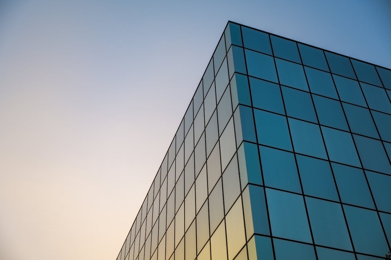 Low angle view of a modern glass facade against a clear sky at sunset, offering a minimalist architectural design.